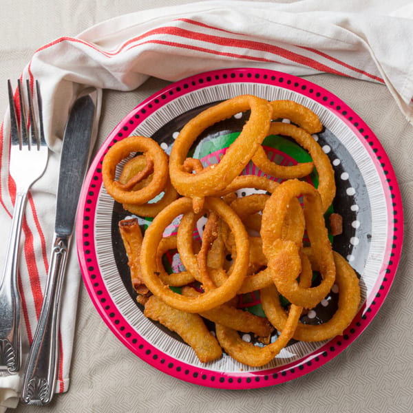 A colorful plate of golden-brown onion rings, with a fork and knife on a striped napkin.