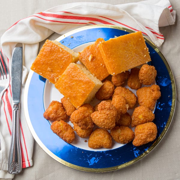 A blue and white plate with golden cornbread squares and crispy fried hushpuppies.