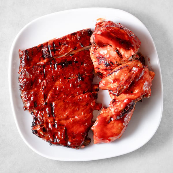 A white plate holds Ribs on the Run's BBQ ribs and chicken, glistening with sauce.