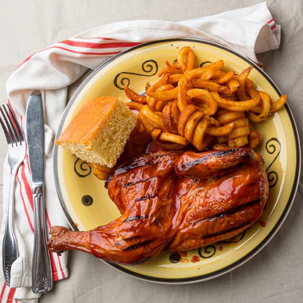 BBQ chicken leg and thigh, curly fries, and cornbread on a yellow plate.