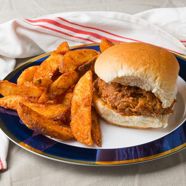 A Ribs on the Run pulled pork sandwich with a side of seasoned potato wedges on a blue plate.